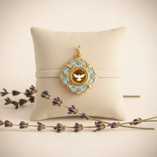 Charger l'image dans la galerie, Médaille dorée Fleur Nabert créations avec colombe blanche sur fond bleu ciel, style cloisonné sur coussin et lavande
